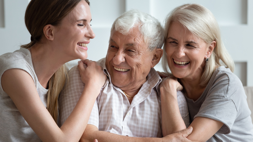 Happy older parents with adult daughter hugging, having fun